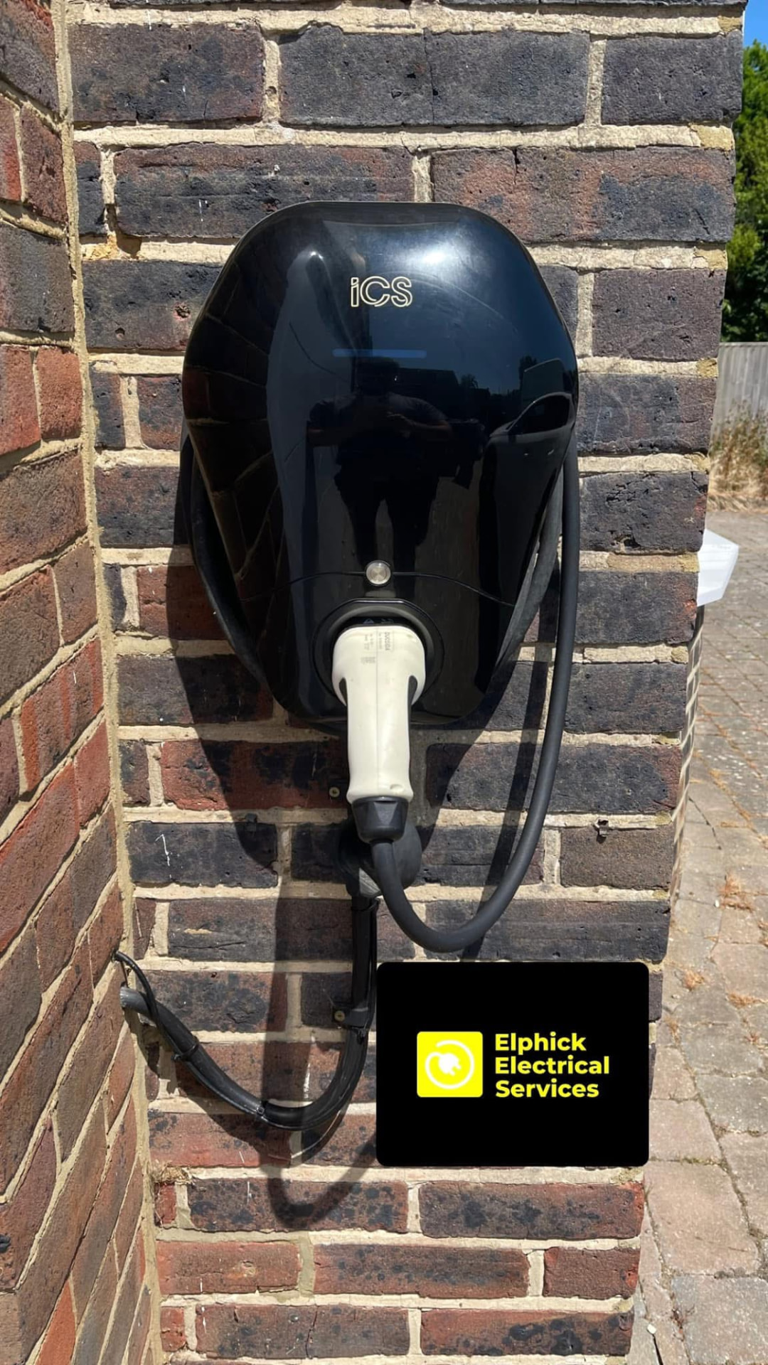 Black EV charge point with connector fitted to a brick pillar